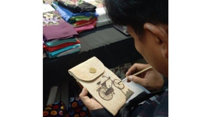 Seorang pelukis dari nasrafa sedang melukis sepeda di pouch untuk Handphone (HP).